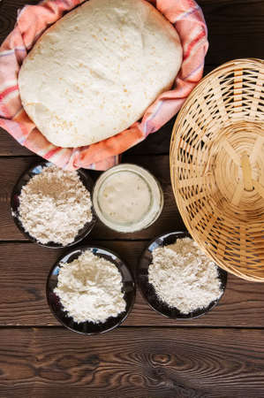 Homemade dough, sourdough in a jar, mix of flours, bread and basket for proof and spatula on a wooden background. Baking concept.の写真素材