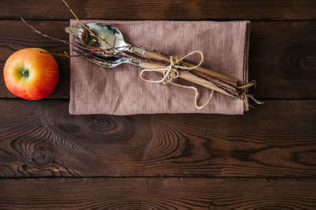 Tree branches, apple, cutlery on a linen sackcloth on a wooden background. Copy space and top view. Autumn mood, Halloween, Thanksgiving, Holiday concept.の写真素材