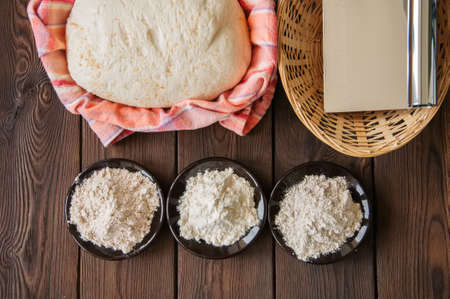 Homemade dough, sourdough in a jar, mix of flours, bread and basket for proof and spatula on a wooden background. Baking concept.の写真素材
