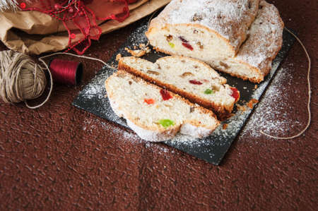 German stollen - Traditional European Festive Baking. Festive Christmas cake with dry fruits and almonds served on stone board on the table with Xmas decorations. Selective focus. Cut. Copy Space.の写真素材