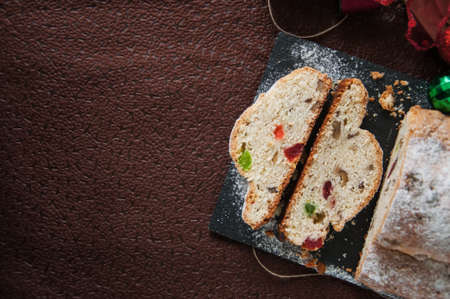 German stollen - Traditional European Festive Baking. Festive Christmas cake with dry fruits and almonds served on stone board on the table with Xmas decorations. Selective focus. Cut. Copy Space. Toned. Top view.の写真素材
