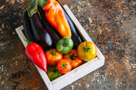 White box with vegetables on a rusty background. Aubergines, bell pepper, tomatoes.の写真素材