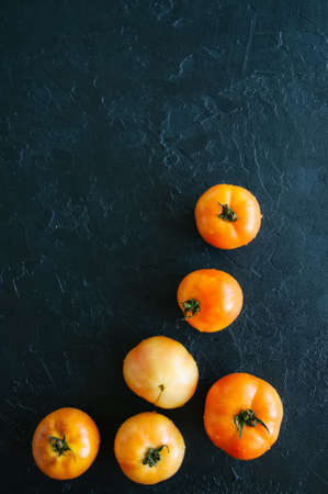 Orange fresh ripe tomatoes on a black stone background. Top view and copy space.の写真素材