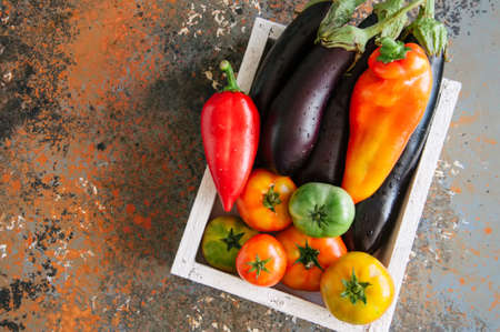 White box with vegetables on a rusty background. Aubergines, bell pepper, tomatoes.の写真素材
