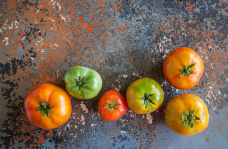 Different sizes of colorful fresh tomatoes on a rusty background. Top view and copy space.の写真素材