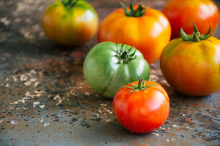 Different sizes of colorful fresh tomatoes on a rusty background. Overhead view and copy space.の写真素材