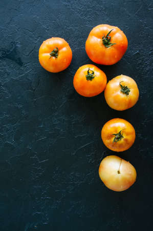 Orange fresh ripe tomatoes on a black stone background. Top view and copy space.の写真素材