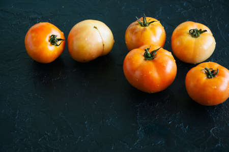 Orange fresh ripe tomatoes on a black stone background. Top view and copy space.の写真素材