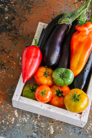 White box with vegetables on a rusty background. Aubergines, bell pepper, tomatoes.の写真素材
