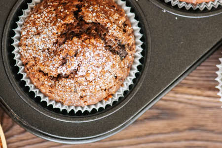 Homemade banana chocolate muffins sprinkled with sugar in a baking form on a wooden background. Top view.の写真素材