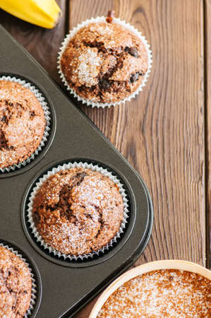 Homemade banana chocolate muffins sprinkled with sugar in a baking form on a wooden background. Top view.の写真素材
