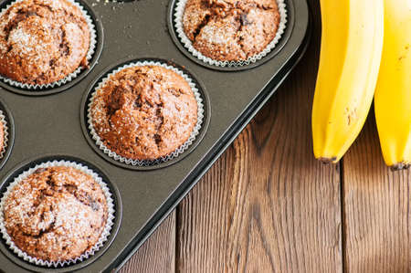 Homemade banana chocolate muffins sprinkled with sugar in a baking form on a wooden background. Top view.の写真素材