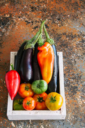 White box with vegetables on a rusty background. Aubergines, bell pepper, tomatoes. Overhead view and copy space.の写真素材