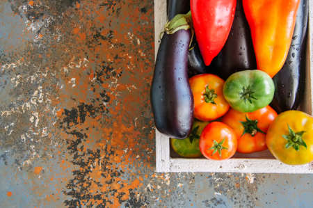 White box with vegetables on a rusty background. Aubergines, bell pepper, tomatoes. Overhead view and copy space.の写真素材
