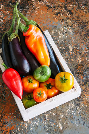White box with vegetables on a rusty background. Aubergines, bell pepper, tomatoes. Overhead view and copy space.の写真素材