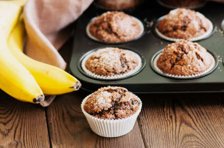 Homemade banana chocolate muffins sprinkled with sugar on a wooden background.の写真素材