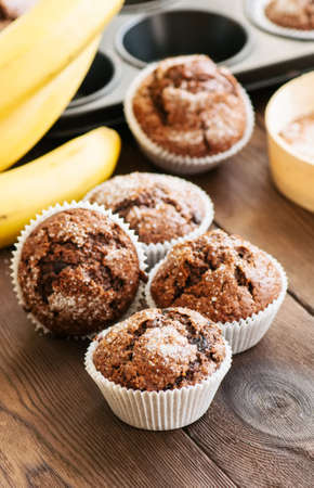 Homemade banana chocolate muffins sprinkled with sugar on a wooden background.の写真素材