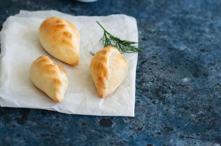 Small mashed potato pasties (hand pies) in a white bowl on a baking paper. Blue stone background.の写真素材