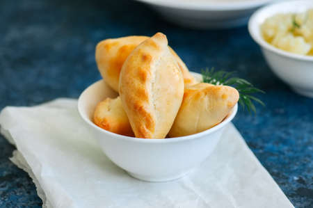 Small mashed potato pasties (hand pies) in a white bowl on a baking paper. Blue stone background.の写真素材