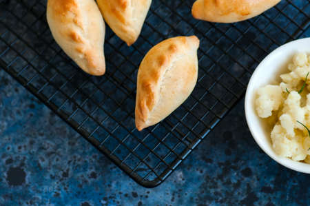 Small mashed potato pasties (hand pies) in a wire rack. Blue stone background.の写真素材