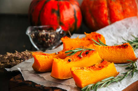 Roasted pumpkin slices with rosemary and dry thyme on a baking paper on a wooden background.の写真素材