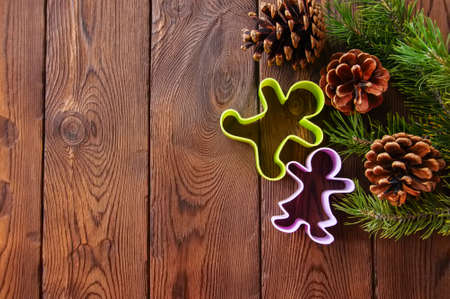 Christmas backdrop. Fir tree branches, cones and gingerbread cutters on a wooden background.の写真素材