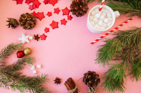 Christmas background with copy space, fir tree branches, hot chocolate with marshmallows, anise, cinnamon, pine cones, red star garland. Pink backdrop.の写真素材
