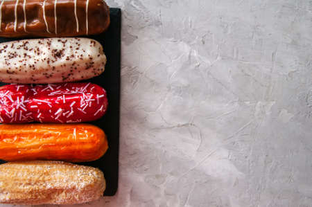 Set of eclairs with different flavors served on a slate board on a white stone background.の写真素材