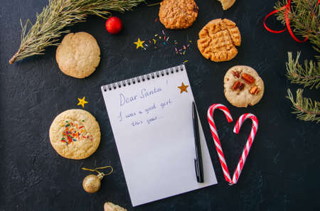 Festive Christmas background. Set of cookies for Santa, candy canes, fir tree branches, balls, white page of notepad with inscription "Dear Santa! I was a good girl this year..." の写真素材