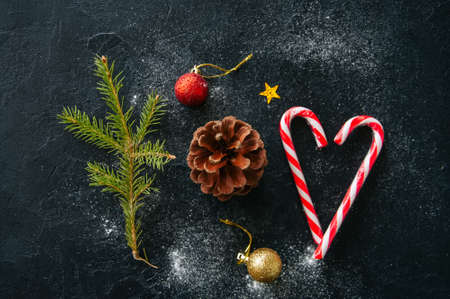 Christmas background. Fir tree branch, cone, candy canes, balls, on a black snowy background.の写真素材