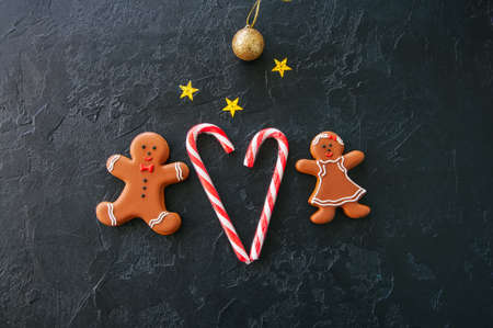 Festive Christmas background, Cookies with image of Gingerbread man and girl candy cane,  stars and ball on a black stone background. Top view with copy space.の写真素材