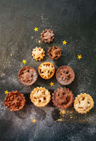 Different sizes of traditional Christmas dessert - Mince pies. Vanilla and chocolate pastry. Black backdrop.Top view.の写真素材