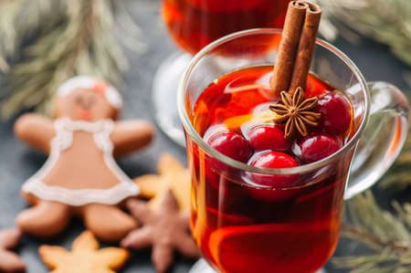 Mulled wine. Christmas hot drink with citrus, apple and spices in a glass cup and gingerbread cookies on a black background.の写真素材