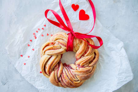 Raspberry jam swirl brioche wreath with red ribbon on a white stone background.の写真素材