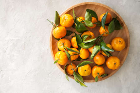 Plate of fresh and juicy tangerines with leaves on a white stone background. Close up and copy space.の写真素材