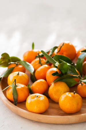 Plate of fresh and juicy tangerines with leaves on a white stone background. Close up and copy...