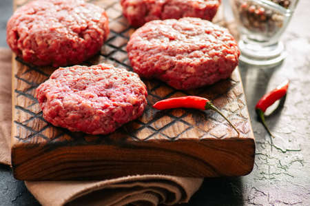 Close up of raw ground meat beef burgers on a wooden board. 