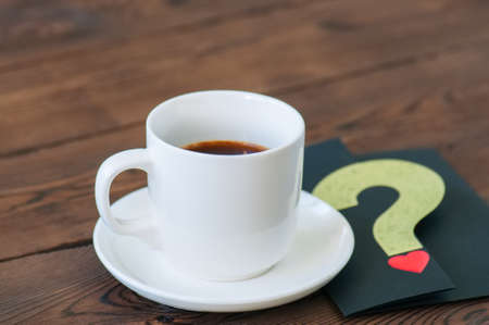 A cup of black coffee and card on a wooden backdrop