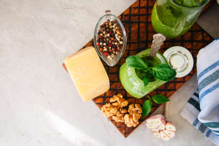 Basil walnut pesto in a jar with raw ingredients on a wooden board. White stone background. Copy space.の写真素材