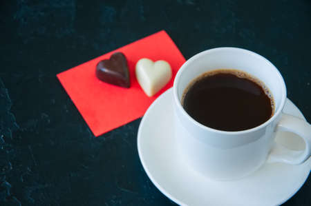 Cup of strong coffee and heart shaped dark and white chocolates on a black background.の写真素材