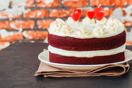 Red velvet cake with cream cheese frosting and heart shaped red candles on a white plate