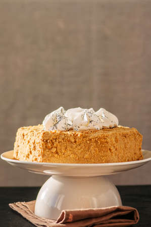 Honey cake with meringue decoration on top served on a white plate on a black backdrop. 