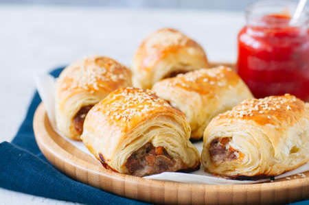 Beef and caramelised onion sausage rolls on a wooden plate with vegemite sauceの写真素材