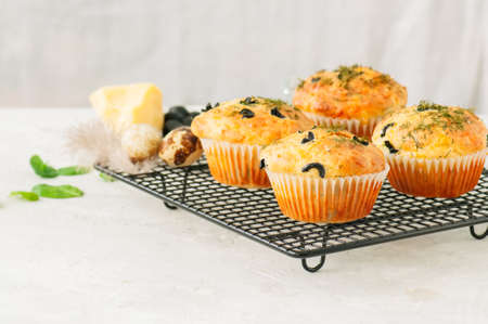 Savory muffins with olives and herbs on a wire rack on a white stone backdrop. Rustic style.の写真素材
