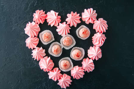 White chocolate and strawberry truffles and pink meringue kisses on black stone backgroundの写真素材