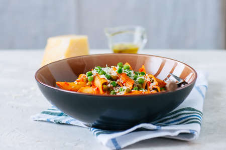 Tomato sauce and green peas penne pasta in a plate on a white stone backgroundの写真素材