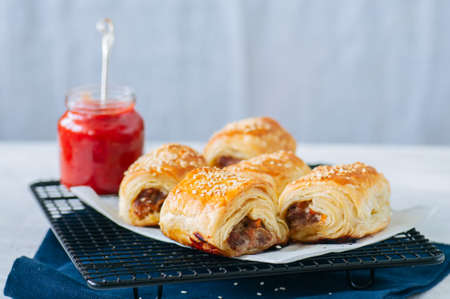 Beef and caramelised onion sausage rolls on a wooden plate with  sauce