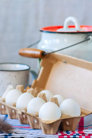 Fresh eggs in a paper container and milk in a can on a wooden background. Stll life. Rustic style.
