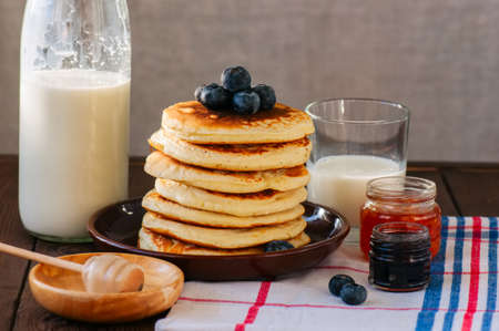 Stack of homemade pancakes with blueberries in a plate, milk and jam preserves in a glass jar.  Rustic style. の写真素材