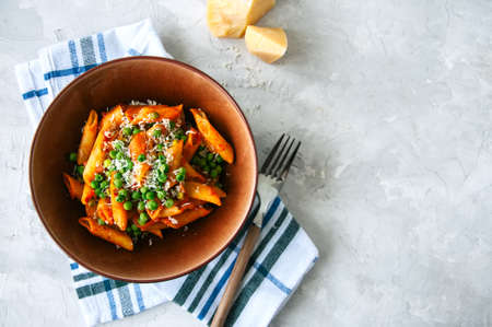 Tomato sauce and green peas penne pasta in a plate on a white stone backgroundの写真素材